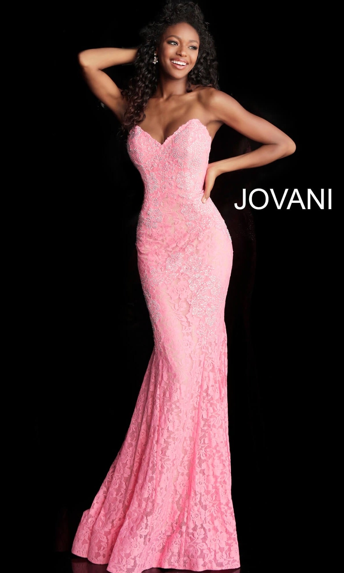 A woman wears a Strapless Long Lace Prom Dress; Jovani 37334, a strapless pink lace gown with a beaded sweetheart neckline and a floor-length skirt.